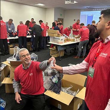 Swire Coca-Cola Food Service and On-Premise (FSOP) team members volunteering by assembling military spouse appreciation kits to support Blue Star Families. The image shows team members in a meeting room, actively participating in the project.
