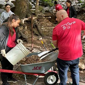 Swire Coca-Cola employees volunteering at Timpanogos Cave National Monument. The team is seen spreading mulch, clearing pathways, and cleaning fire rings as part of their efforts to beautify the popular picnic area.